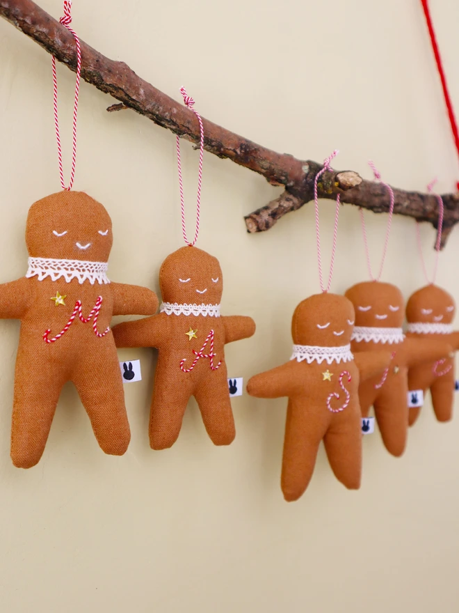 Brown linen gingerbread man christmas tree ornament with a letter hand embroidered in candy cane colours, star shaped sequin, crochet cotton lace around the neck, smile embroidered in white and candy cane colour string to hang. 