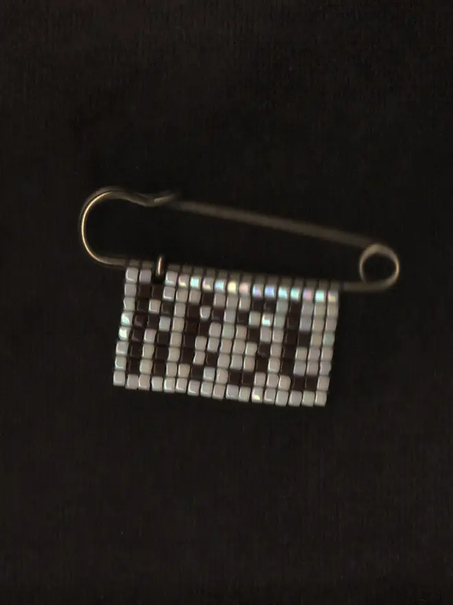 'lingua iii' beaded rest pin. a beaded pin badge with the word rest in brown lettering on a pearl background.