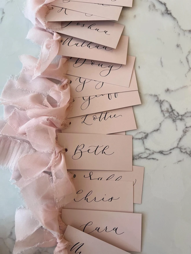 Personalised Calligraphy Wedding Pink Place Cards, pink wedding cards with pink ribbons grouped together. 