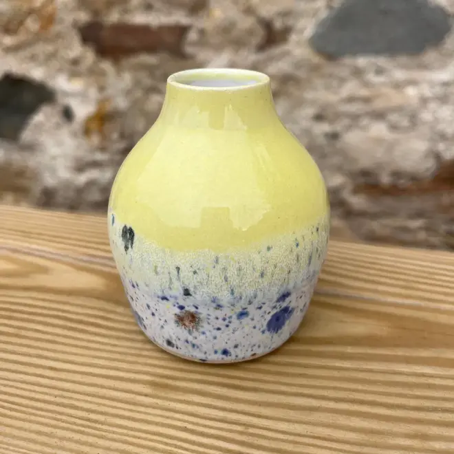 Shoreline Bud Vase, a colourful vase placed on a wooden surface against a brick backdrop. 