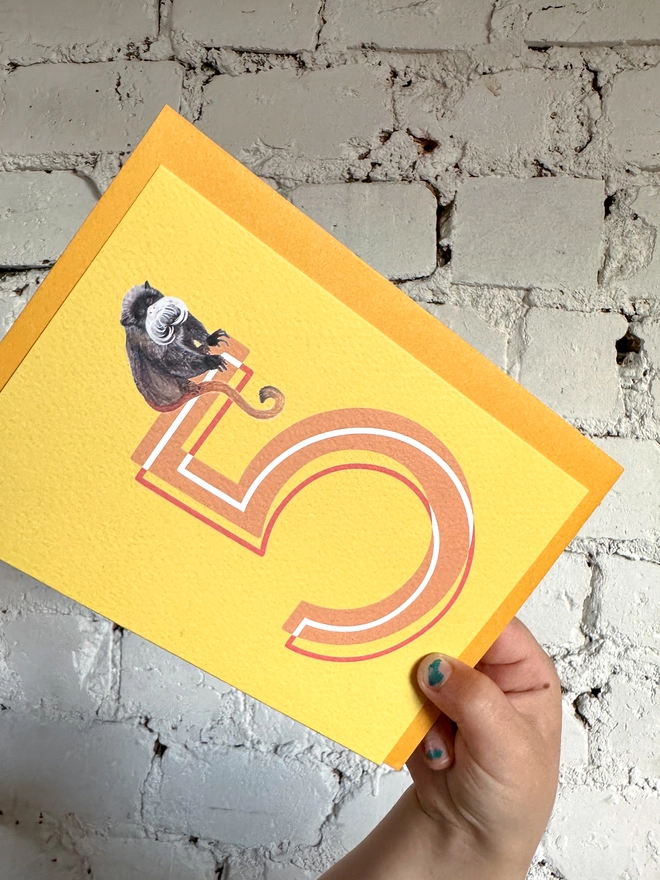 bright yellow card featuring a big orange number 5 and an illustration of an emperor tamarin with a bright yellow envelope