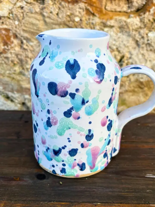 Sweetpea Medium Jug, a colourful jug placed on a wooden surface against a brick backdrop. 