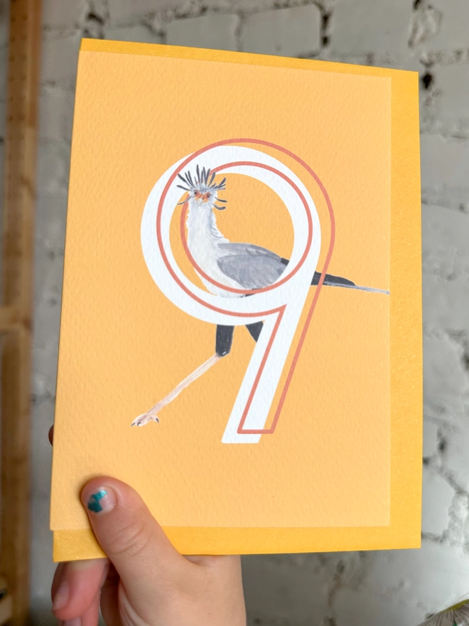 Bright yellow card with an illustration of a secretary bird and a big white number 9, with a yellow envelope