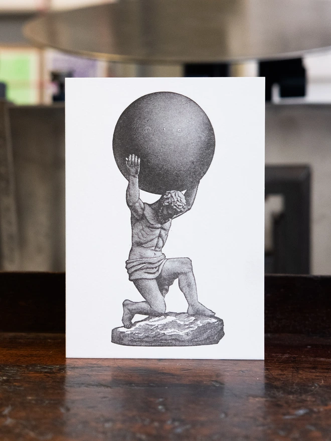 Letterpress card with design printed thereupon. The Titan Atlas holding one of the celestial spheres, shaded with parallel lines.