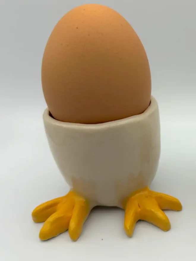 egg cup with yellow feet, holding single brown egg