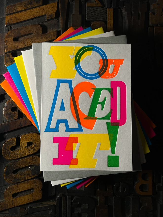 Colourful typographic letterpress card with bold overlapping neon letters spelling ‘You Aced It!’, perfect for celebrating exam success.