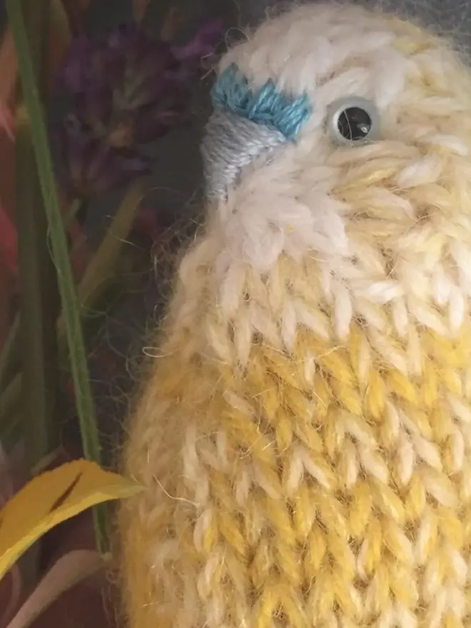 Colourful Hand Knitted Budgerigar, a yellow colourful birds sitting on a wooden surface. 
