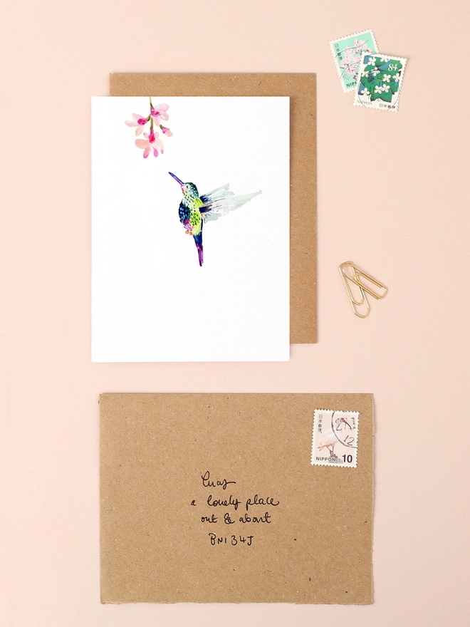 A graceful illustration of a vibrant hummingbird in mid-flight, its iridescent feathers shimmering in hues of green, blue, and pink. The bird hovers delicately against a soft, neutral background, exuding a sense of joy and freedom. The minimalist design captures the elegance of the hummingbird, making it a perfect choice for sending heartfelt messages on birthdays, anniversaries, or as a thoughtful note to brighten someone's day.