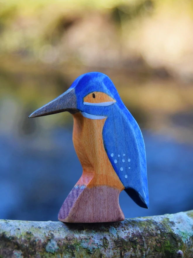 wooden toy kingfisher on twig branch in front of river