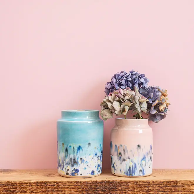 Shoreline Large Vase, a colourful vase placed on a wooden surface in front of a pink backdrop. It is accompanied by a small vase. 