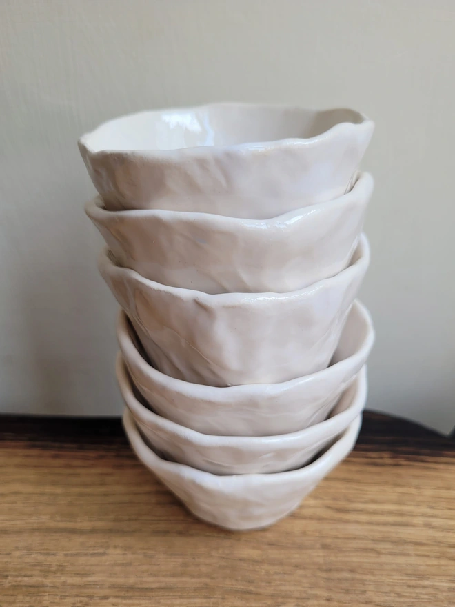 a stack of white ceramic hand made small pots on a wooden surface