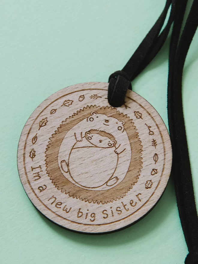 Wooden medal etched the the words "I'm a new big sister" underneath 2 sibling hedgehogs