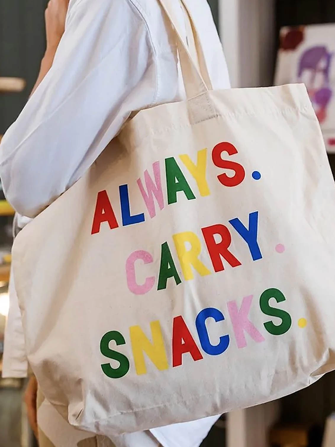 A person carrying a canvas tote bag with Always Carry Snacks slogan