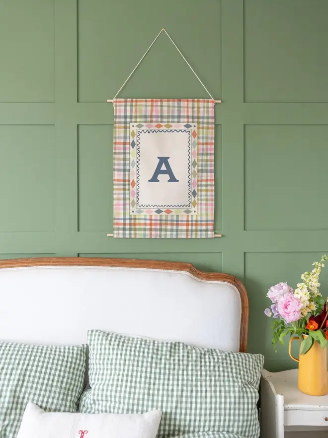 Rainbow Gingham Initial Fabric Banner, against a green wall. 