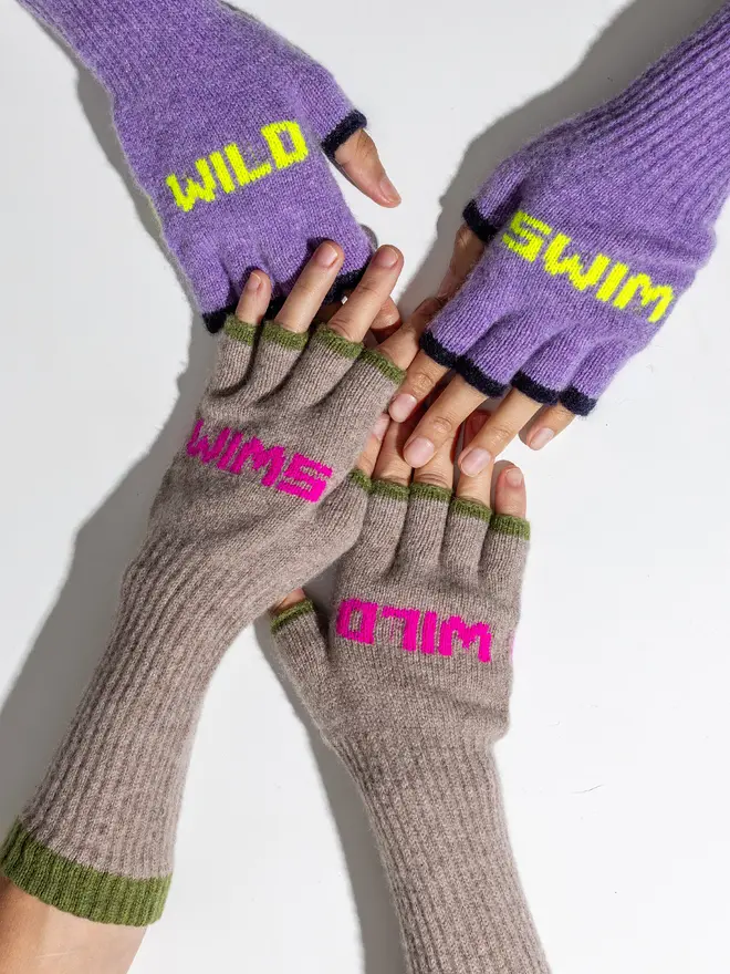 two model reaching across a table to hold hands. Both models are wearing our wild swim mittens, one is wearing parma violet and the other is wearing mushroom 