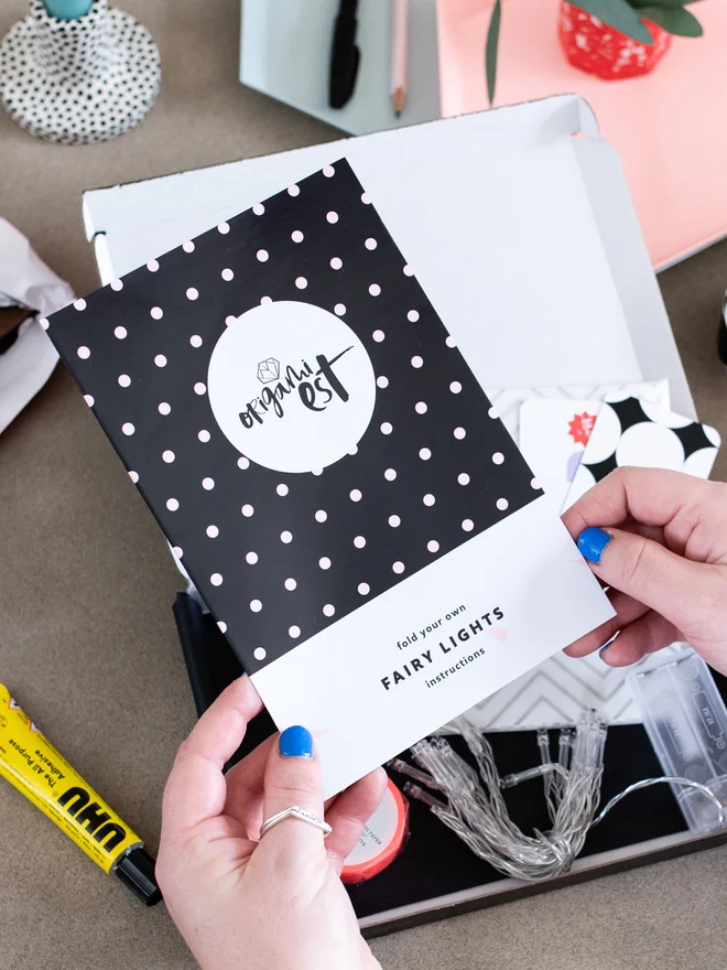 Woman's hands holding origami instruction sheet with kit open on table below
