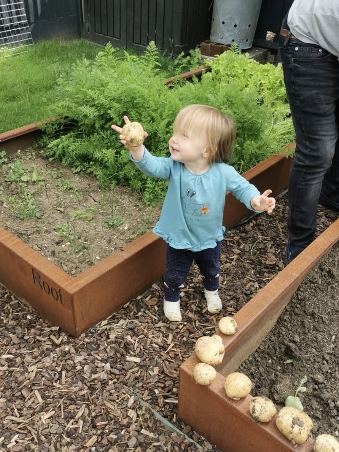 Braybrooke Corten Raised Bed Planters, planter in garden with produce growing, with child planting seeds. 