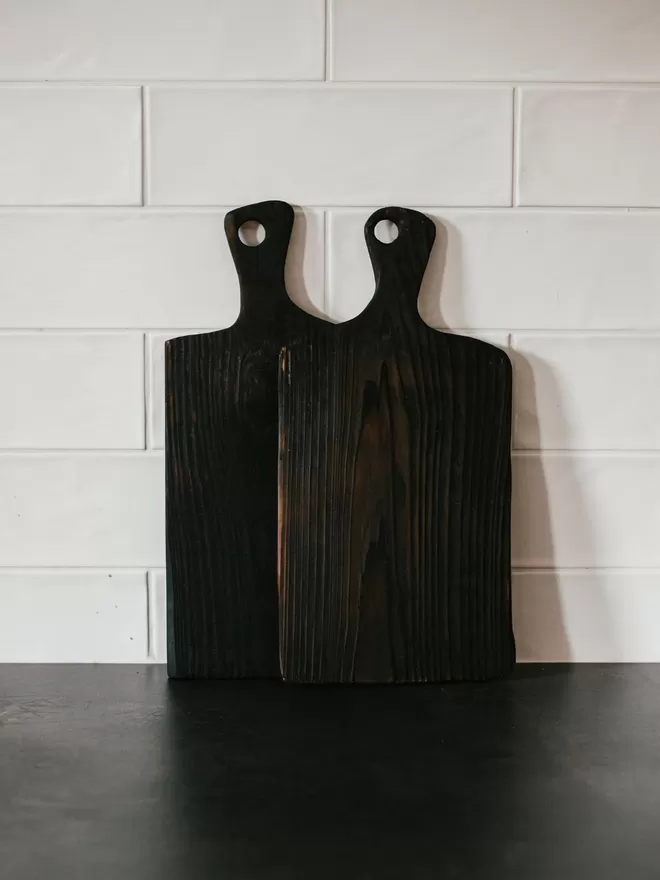 ‘Pass The Cheese!’ Round Handle Charred Black Serving Board  seen on a kitchen counter.