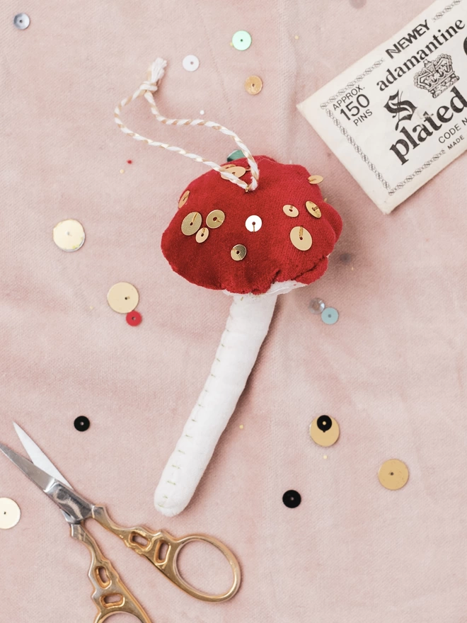 A velvet and sequin toadstool ornament on a pink cloth