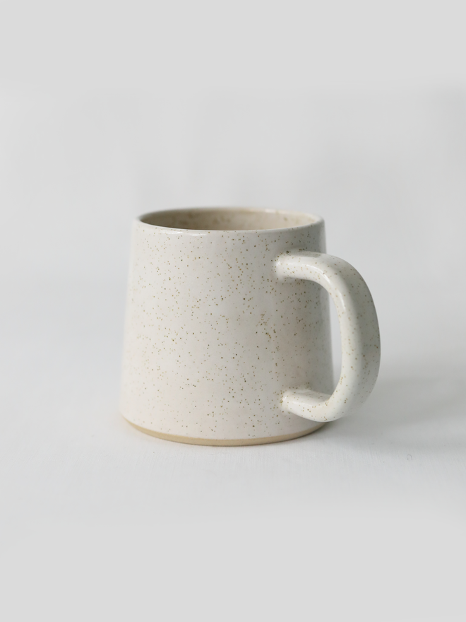 A handmade ceramic standard mug in glossy pepper white glaze with a chunky loop handle, photographed against a plain light grey background
