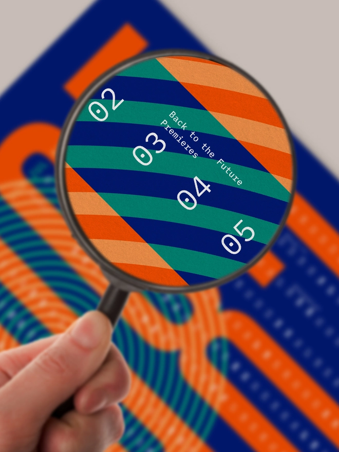 Hand with magnifying glass, focus on a printed poster in blue and orange with highlighted date "03" and text "Back to the future released"