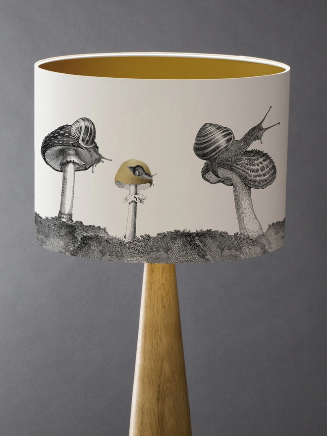 Drum Lampshade featuring snails sitting on mushrooms and toadstools with a gold inner on a wooden base 