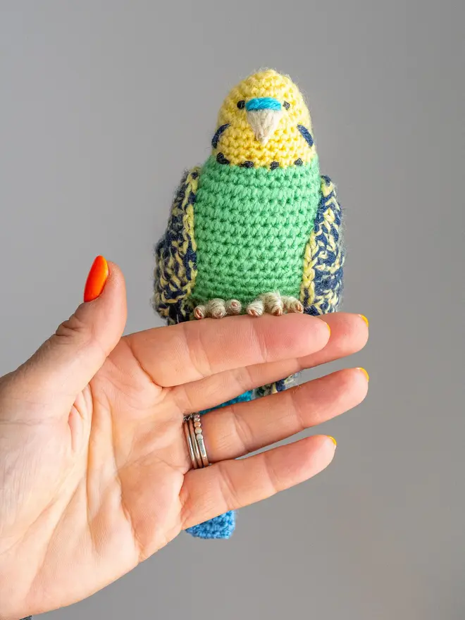 Budgerigar Hand Crocheted Figure, a green  crocheted bird sitting on a wooden poll. 