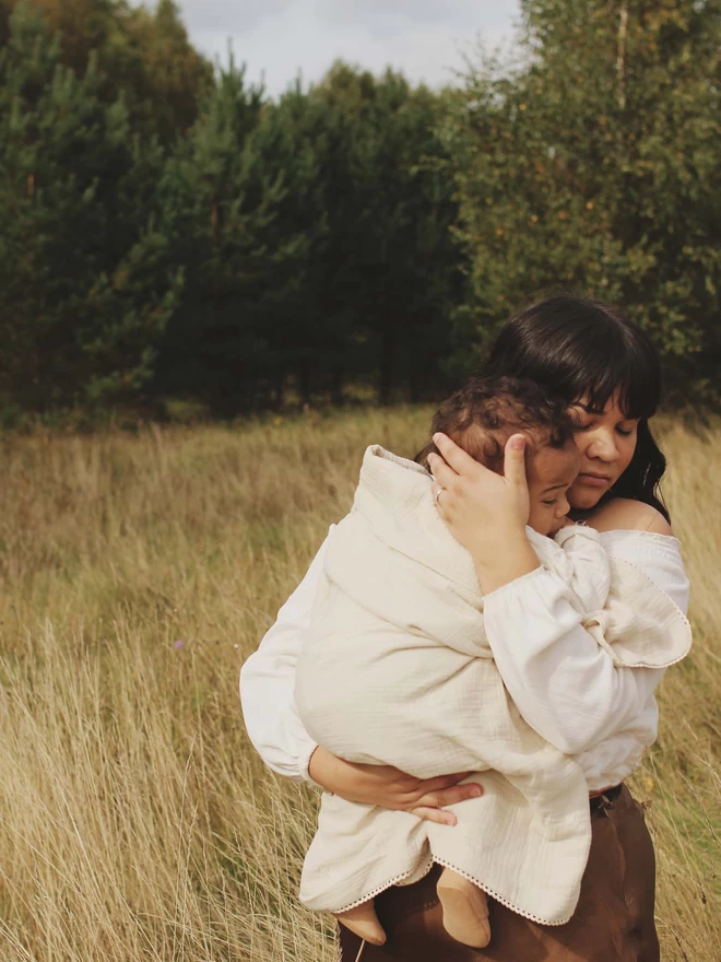 A mom and her child wrapped in a muslin blanket grasslands