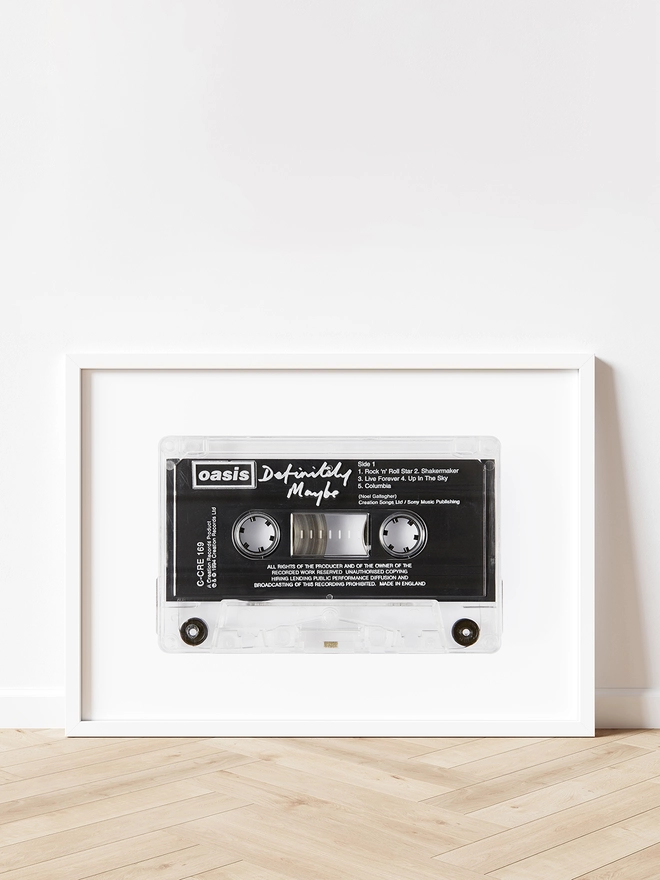 oasis definitely maybe cassette tape print. framed print propped up against white wall and wooden floor.