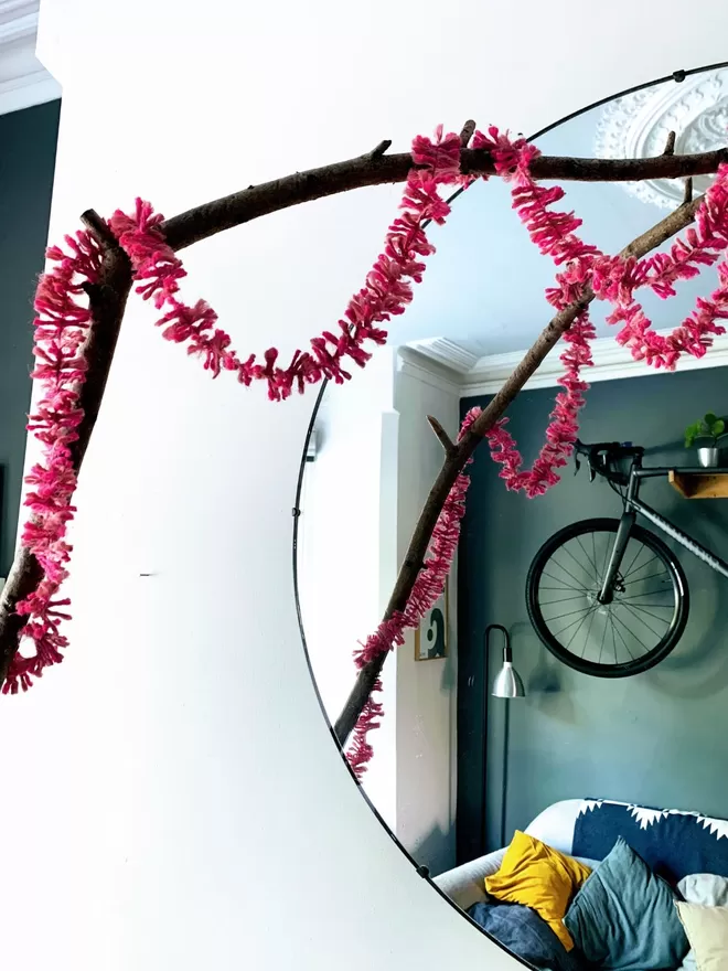 Bright pink jute string tinsel looped over a branch reflected in a mirror showing a contemporary living room