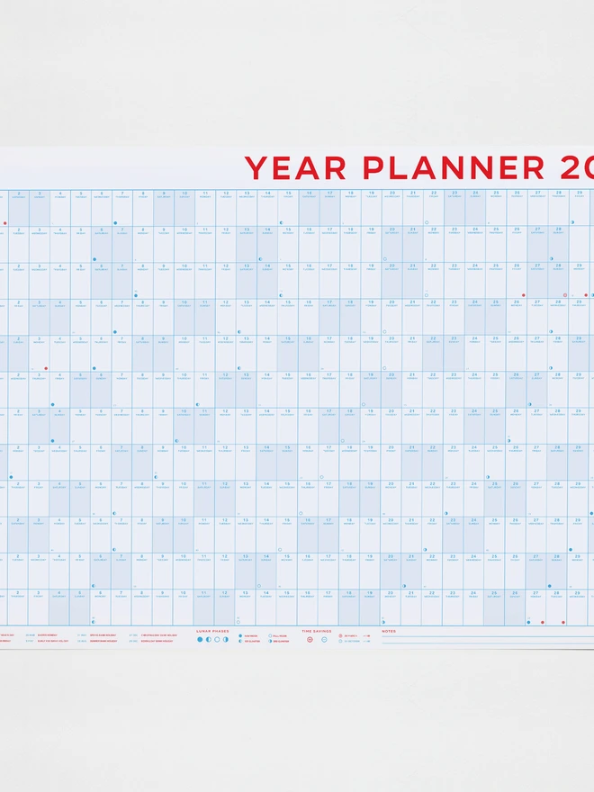A large 2027 wall planner by Crispin Finn, viewed horizontally. The single-sheet calendar features a grid layout for all 12 months, printed on 100% recycled paper using a striking retro two-tone red and blue color scheme, with weekends prominently highlighted in red.