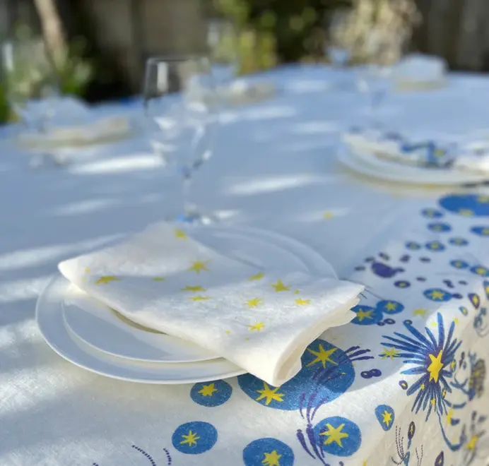 Stars Napkins In White (Set of 4). White cloth napkins with scattered yellow star prints placed in a plate. 