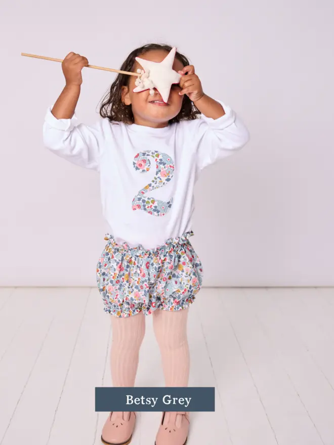 a little girl wearing a white birthday t-shirt with a number 2 cut from liberty floral print on the front