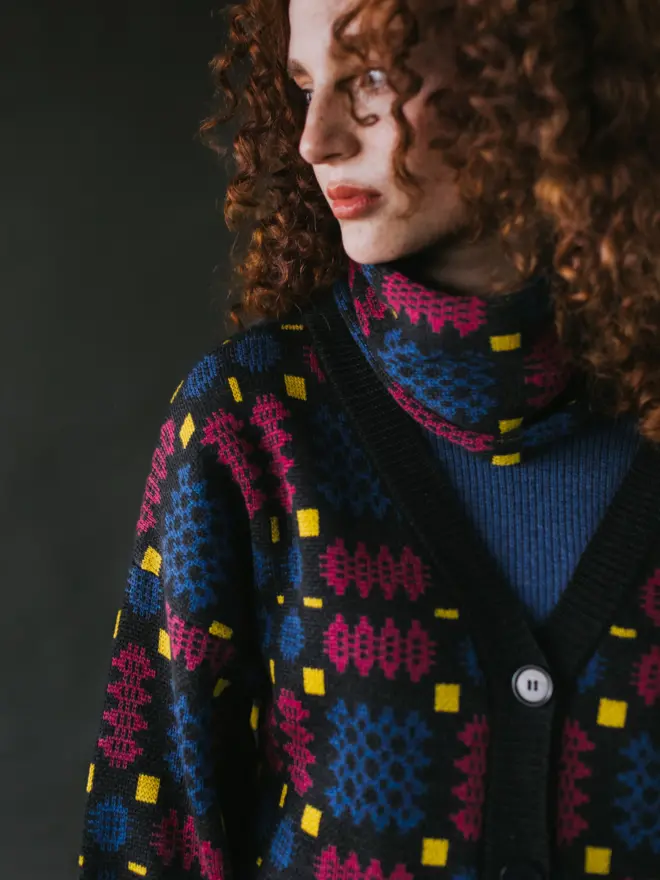 Model wearing pieces from MABLI's 'Carthen' collection, featuring the Carthen Cardigan in the vibrant 'Fireworks' colour-way. The design showcases bold, colourful patterns inspired by traditional Welsh blanket tapestry.