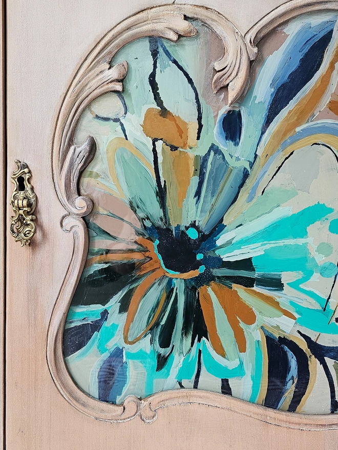 Close up view of hand-painted floral design in navy blue, turquoise, orange and cream on a lime-washed restored vintage cabinet by Chloe Kempster