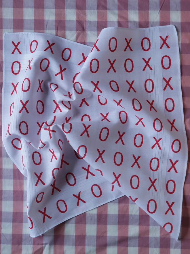 A Mr.PS Hugs and Kisses handkerchief printed in red on a pink gingham tablecloth