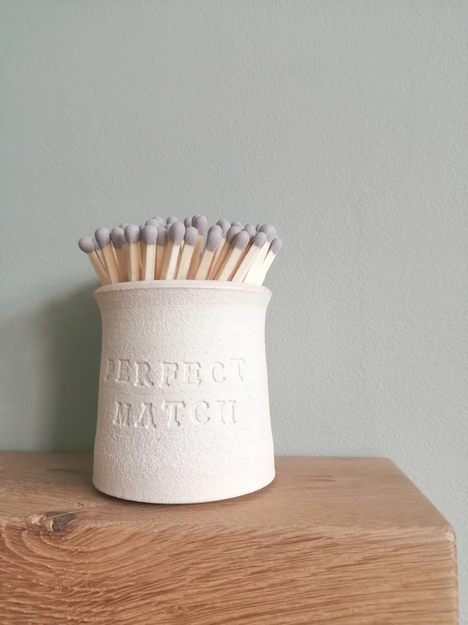 Match pot on wooden fireplace with grey tip matches inside. Perfect Match stamped on the outside