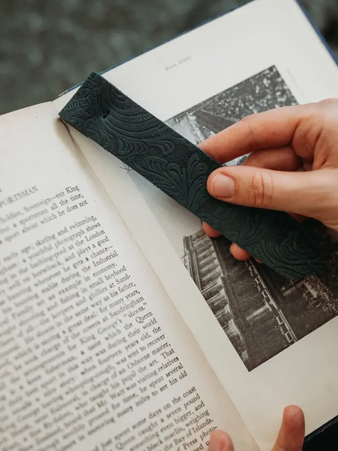 botanical leather bookmark. a dark green bookmark held between two pages of a book.