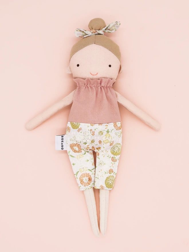 Taupe hair girl doll with light skin, pink top and floral trousers. 