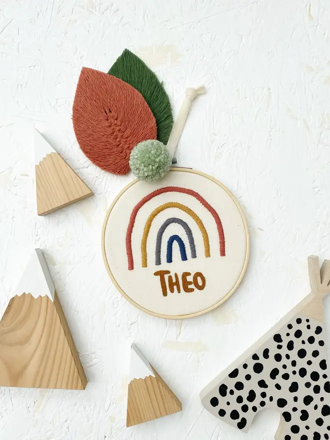 personalised name and rainbow embroidered hoop. cotton hoop embroidered with the name theo and a red, yellow and blue rainbow.