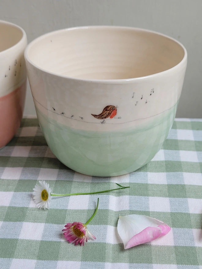 green glazed ceramic pottery tumbler with a robin red breast bird  on a green gingham tablecloth