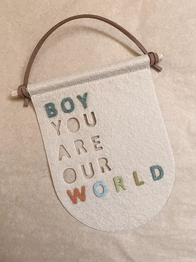Cream flag saying boy you are our world with multicoloured letters for world.
