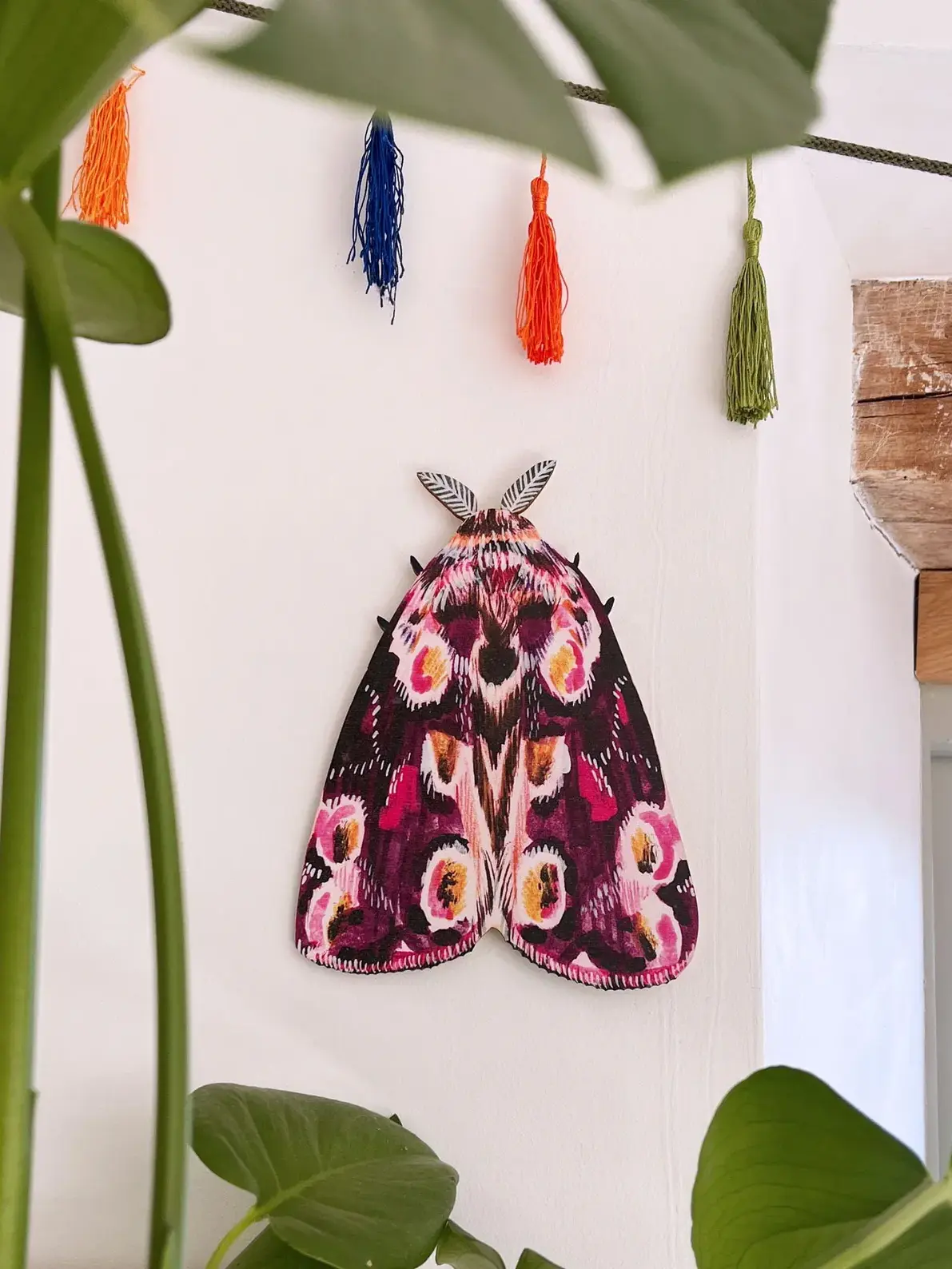 large wooden moth wall decoration. large pink wooden moth decoration hung on plain white wall.