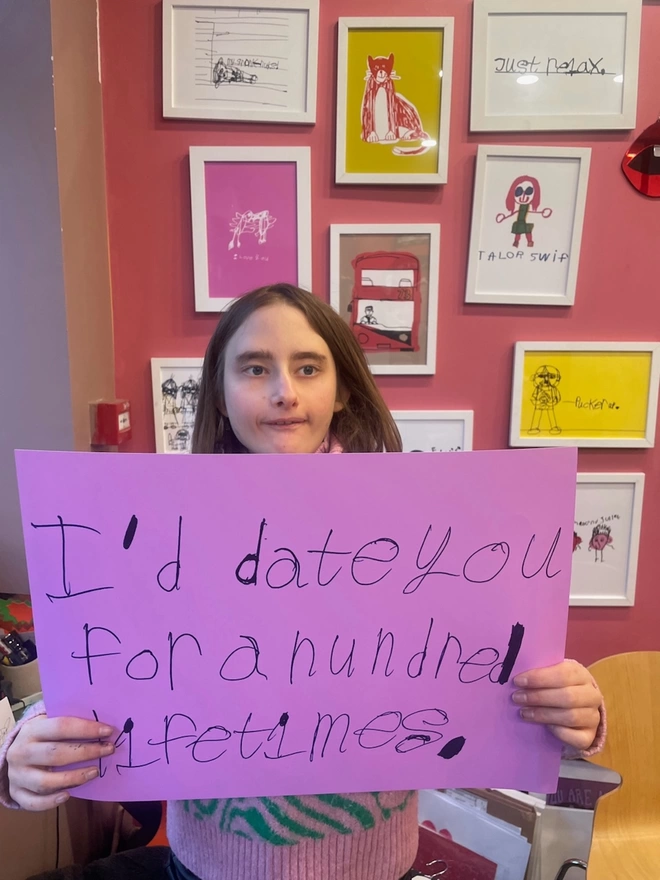 Piper is holding up her note which is in a3 with her unique font in blue ink on a bright pink background