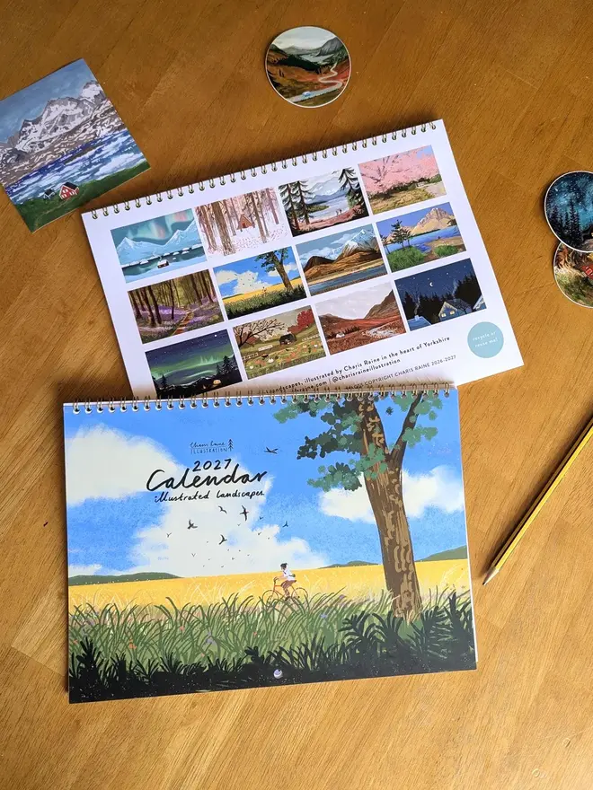 Illustrated landscape calendar by Charis Raine featuring a cyclist though yellow and green fields, with a tree and blue sky
