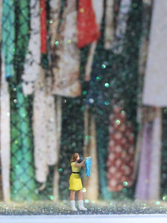 A tiny woman holds up a sparkling blue item of clothing set against a sparkling interior of an overflowing wardrobe (close up)