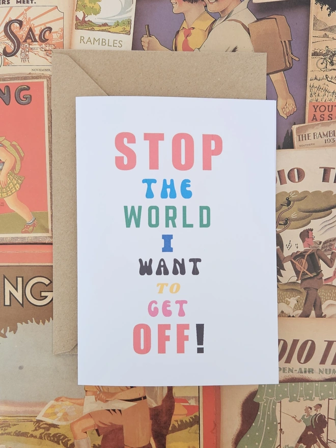 A mindful empathetic greeting card that says stop the world I want to get off in colourful fonts on a white card photographed on a background of old walking destinations