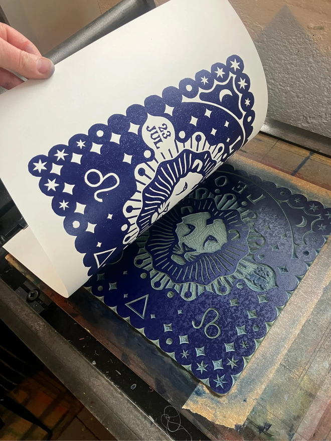 leo zodiac lino cut. a linocut lion and zodiac symbols printed on a blue background.