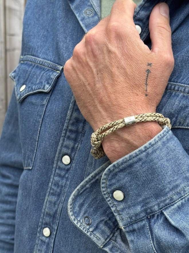 men's personalised drift paracord bracelet. a close up of a man's arm in a denim shirt wearing a sand coloured paracord bracelet.