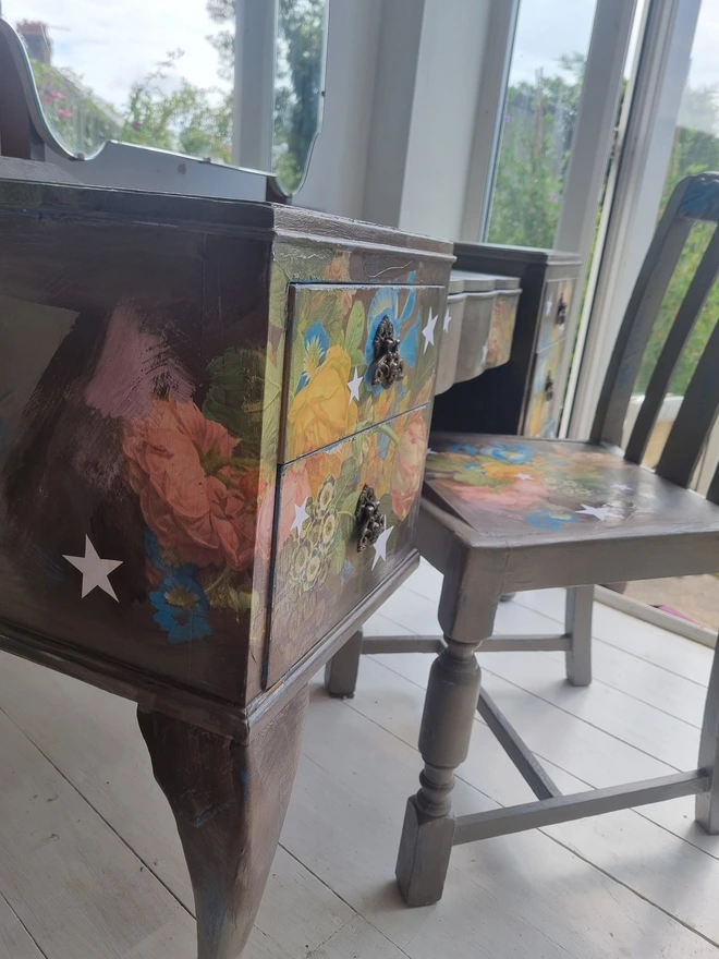 Vintage painted dressing table and chair. Painted in coffee grey and decorated using layered antique florals with yellow and blue accents and finished with hand-cut white paper stars. Text reads in blue 'think happy thoughts'. Heavily distressed finish.